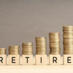 Retire word in wooden blocks with coins stacked in increasing stacks. Retire in wealth concept. Copy space